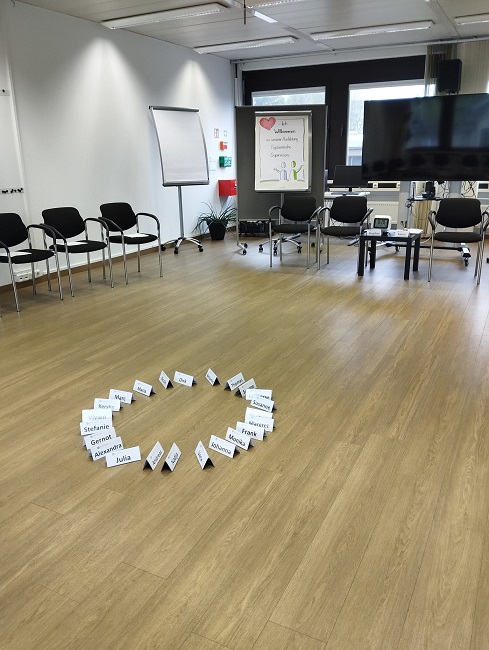 Seminarraum links Stühle, in der Mitte Namensschilder hinten Flipchart und Bildschirm