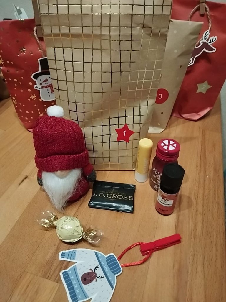 Beutel mit Nummer 1, davor ein Wichtel, Süßigkeiten, Lippenbalm und Duftöl