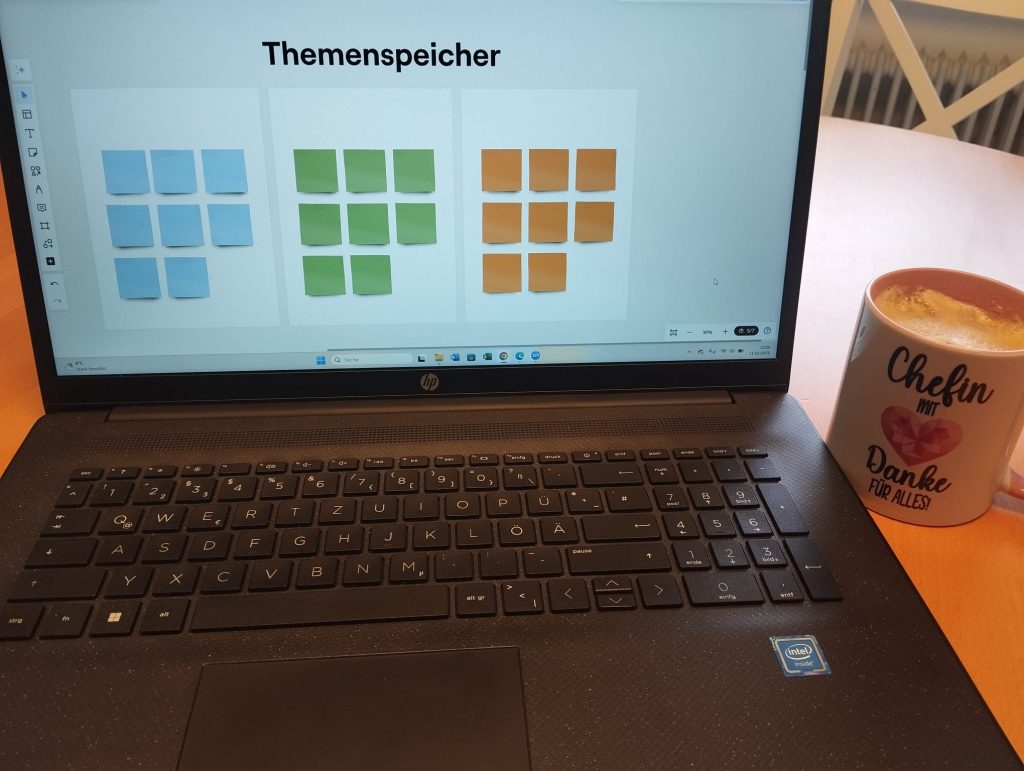 Laptop offen mit dem Bild (Themenspeicher", daneben eine Tasse Kaffee