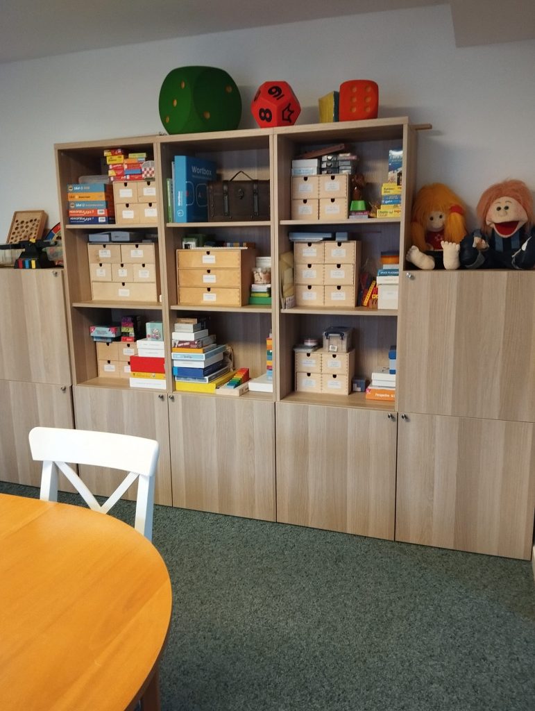 ein Schrank mit vielen Schubfächern oben vier Würfel rechts zwei Handpuppen