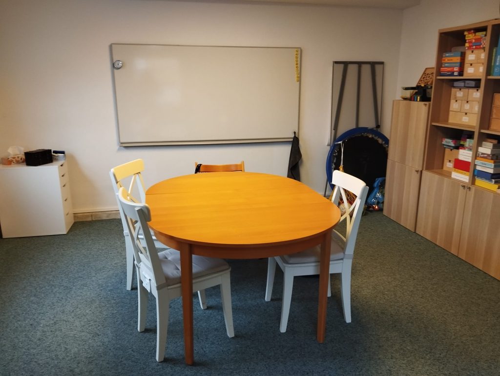 in der Mitte ein ovaler Tisch mit vier Stühlen an der wand ein Whiteboard rechts ein Schrank